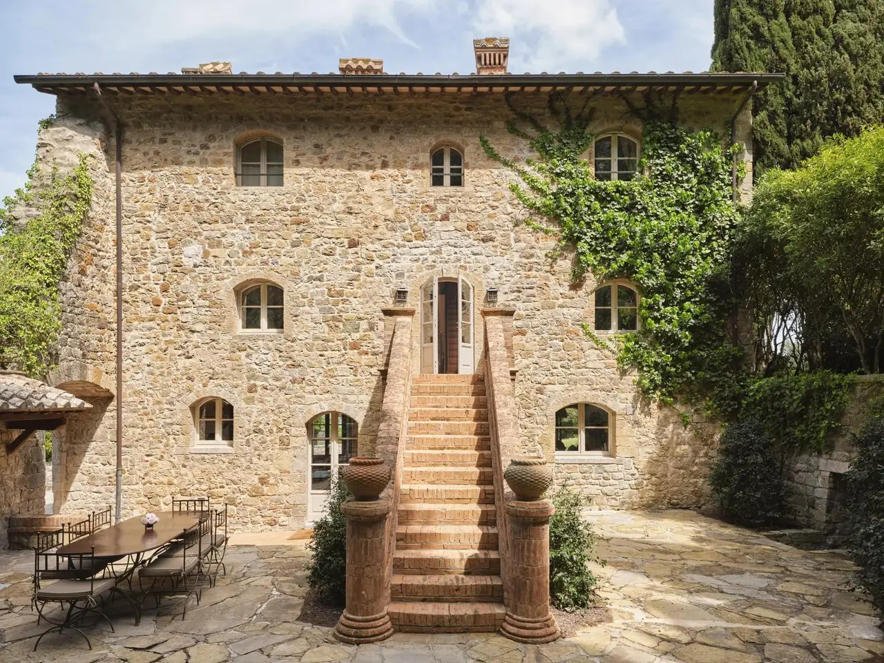 Villa Castello’s stone front, its outside staircase between 2 urns and a table laid in the courtyard.