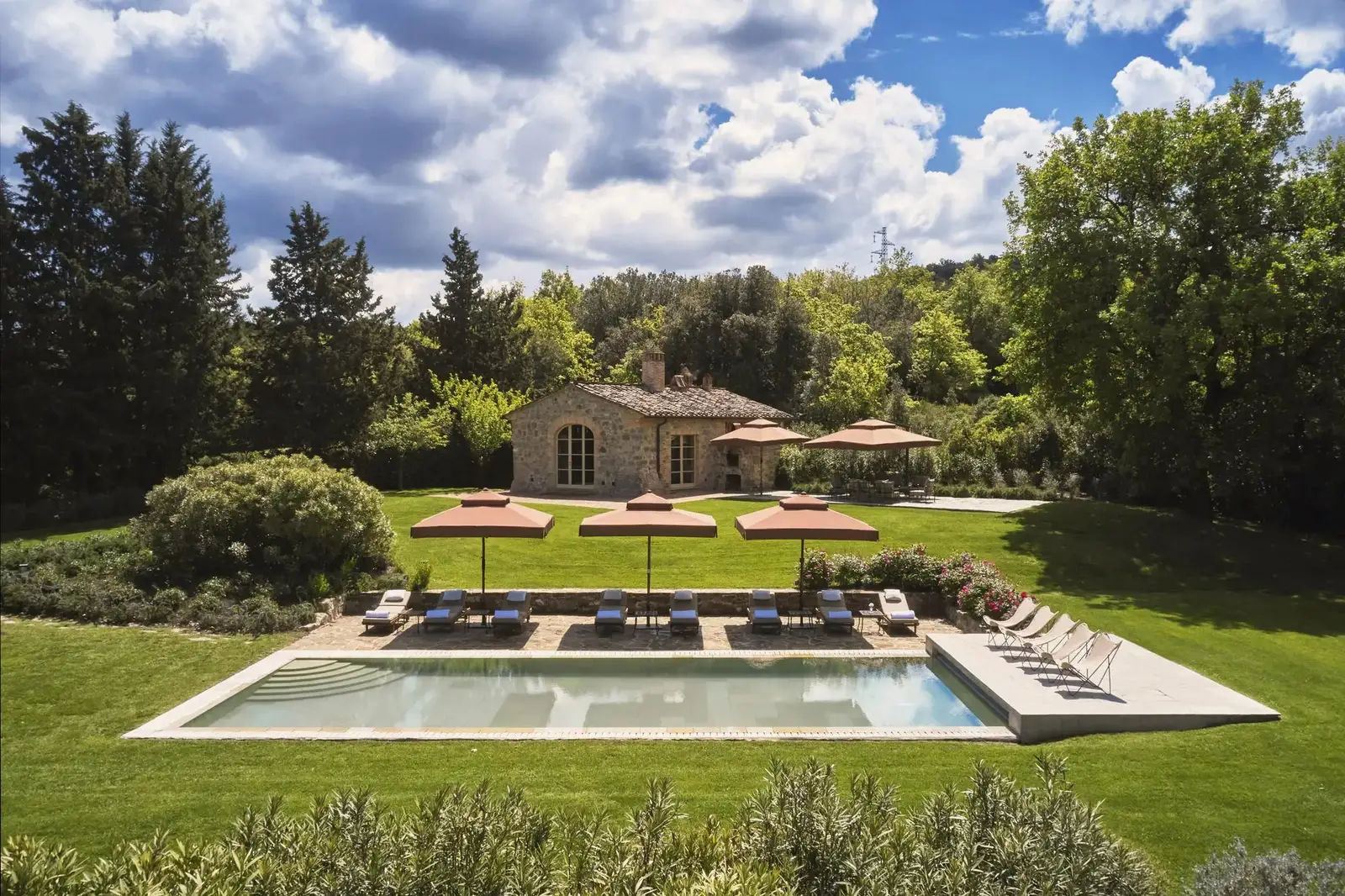Villa Gauggiole’s pool on the lawn, loungers under the parasols and the stone house among the trees.