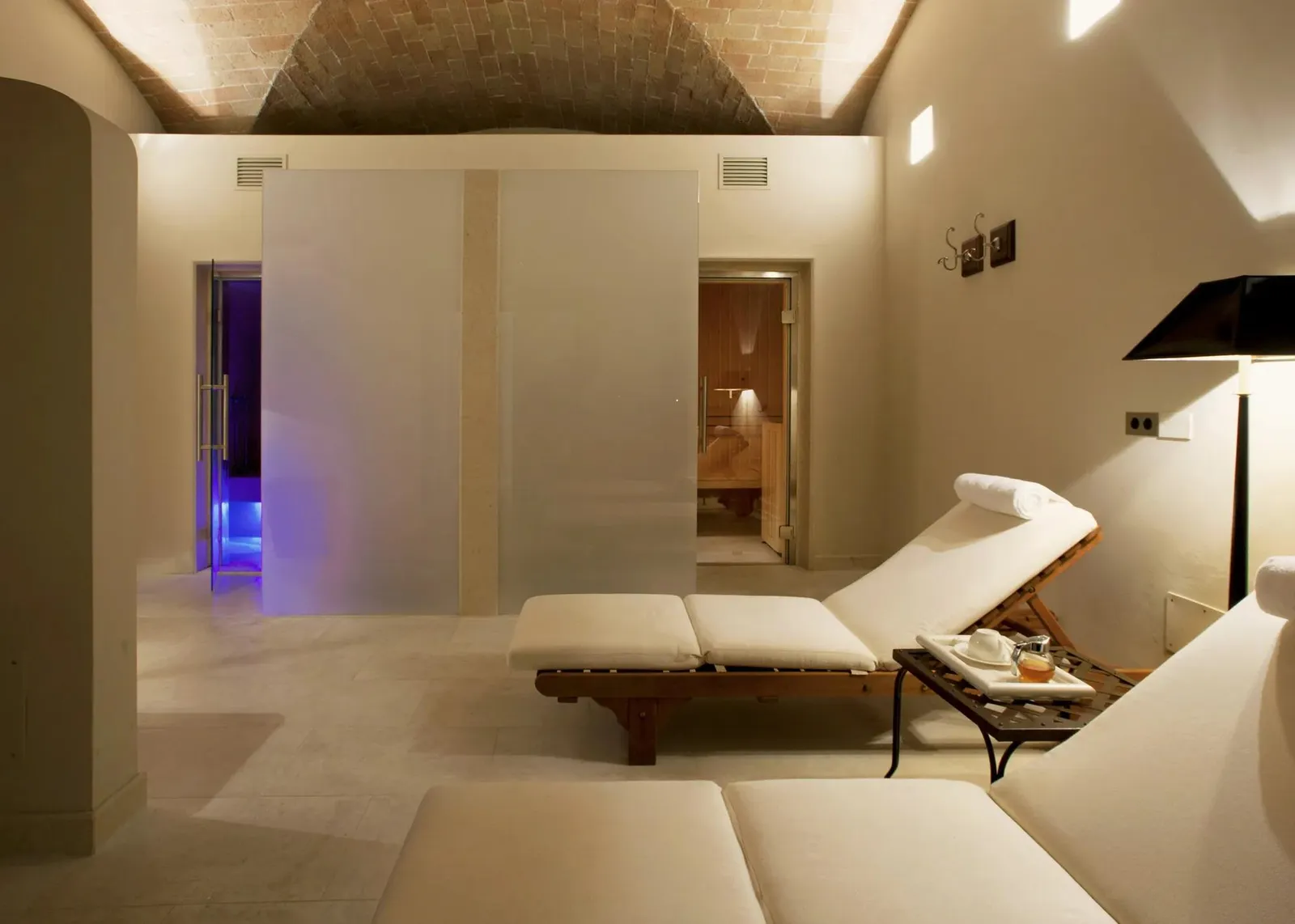 The spa’s wet area: the sauna and steam-bath doors, 2 wooden loungers and low vaults of pale stone.