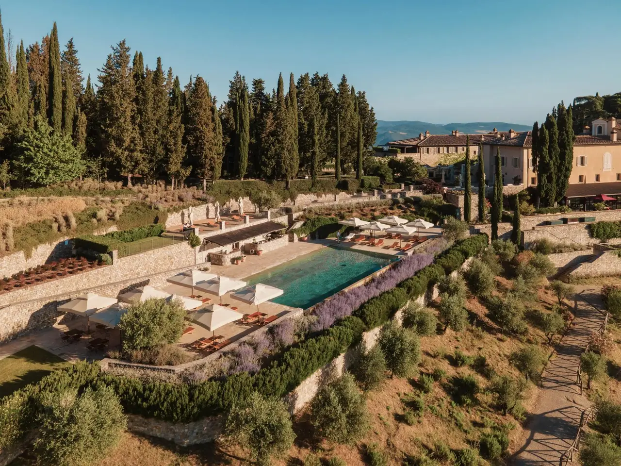 The borgo from above: the terraces, the infinity pool among olives and cypresses, and the hills falling away to the valley.