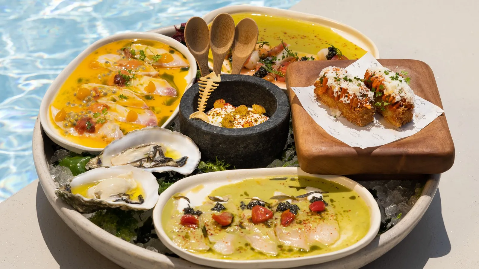 A platter at Meraki from above, with raw fish, oysters and fried croquettes, set on the edge of the pool.