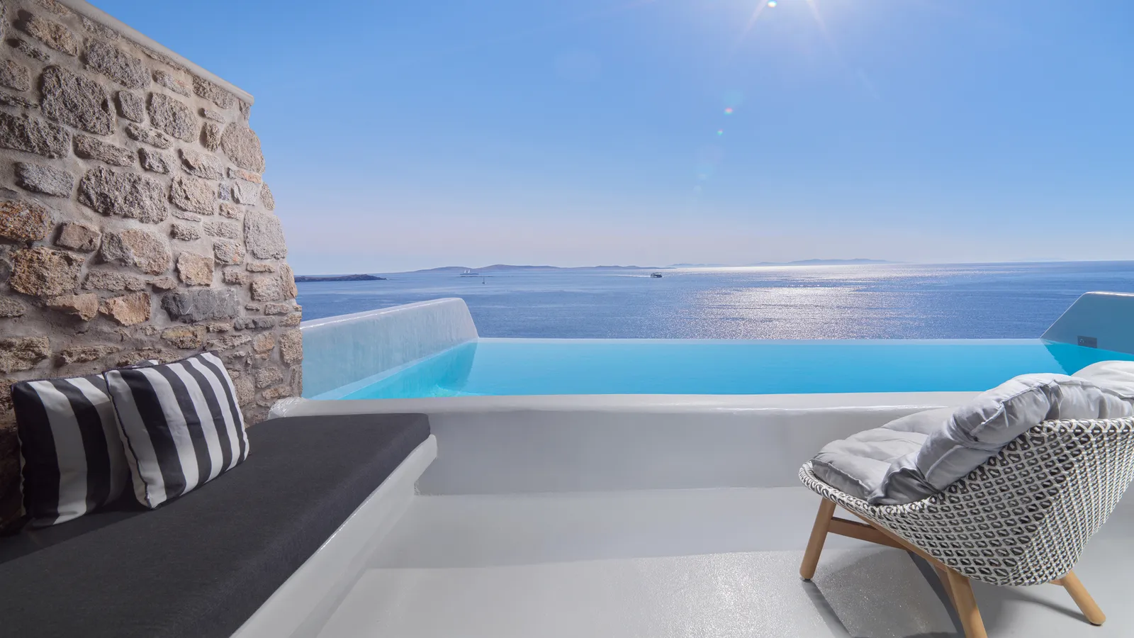 A terrace with a private infinity pool, a bench with striped cushions under a stone wall and a wicker chair.