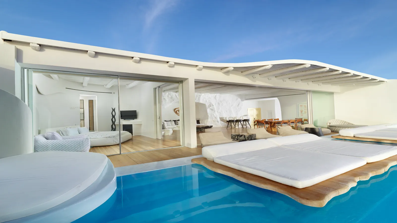 The Diamond Villa by day: the pool with daybeds on decks, an undulating white canopy and the living room open behind the glass.