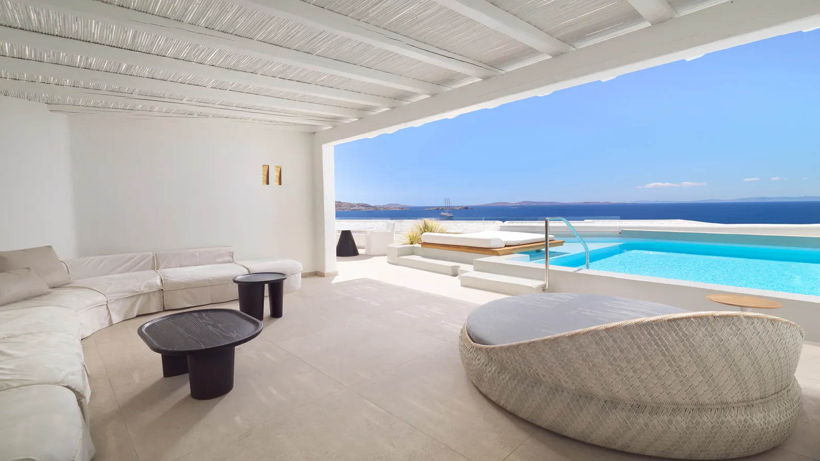 The covered living area of the one-bedroom Golden Villa, with a curved sofa and a wicker daybed facing the private pool and the sea.