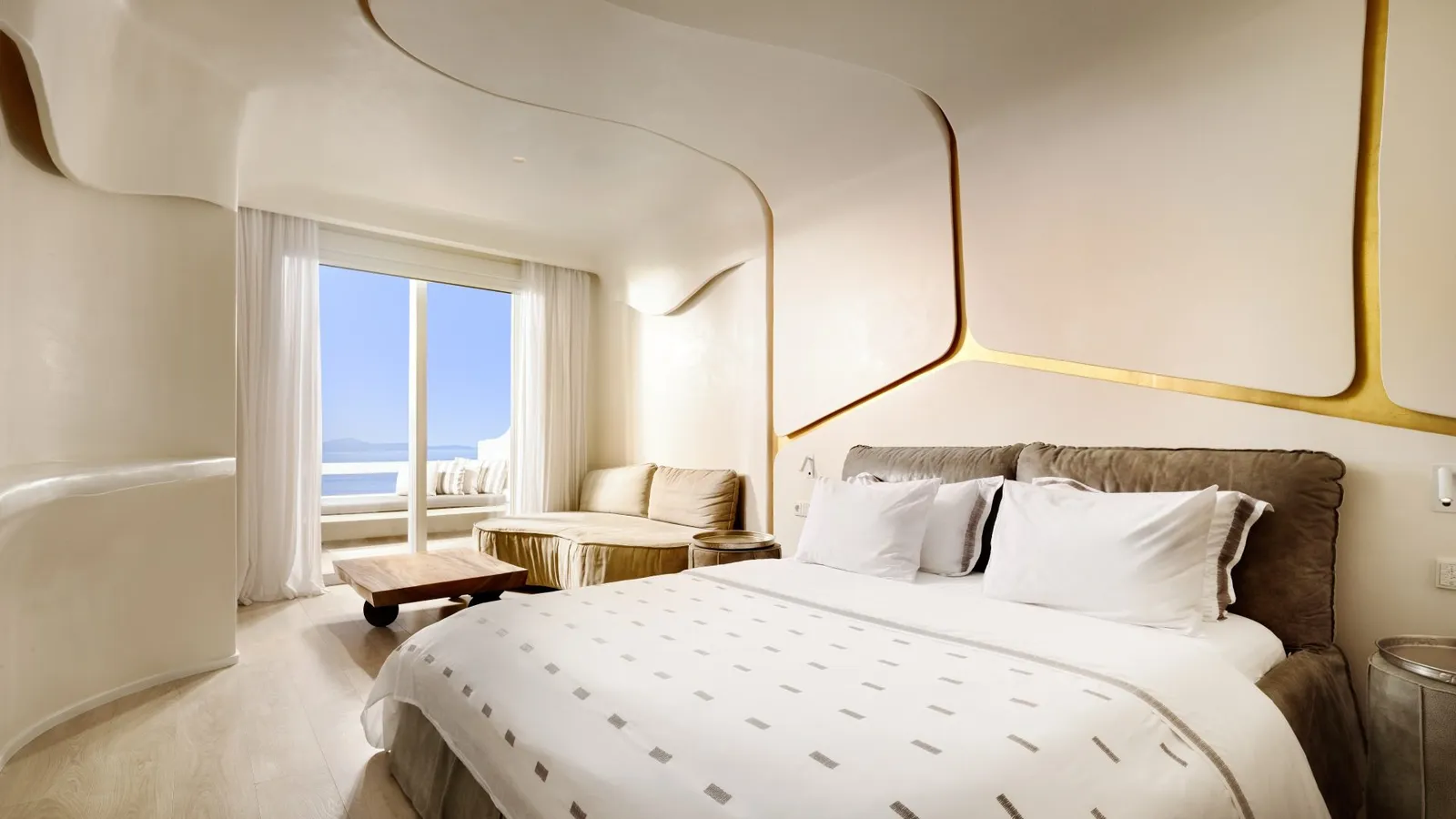 A Junior Suite: the bed with its leather headboard, curved walls edged in gold and a sitting area by the window.