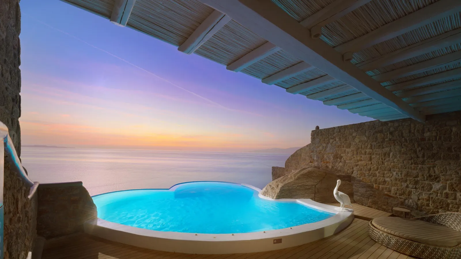 The heart-shaped pool of the Platinum Villa at twilight, under a reed canopy, with rock to the right and the sea.