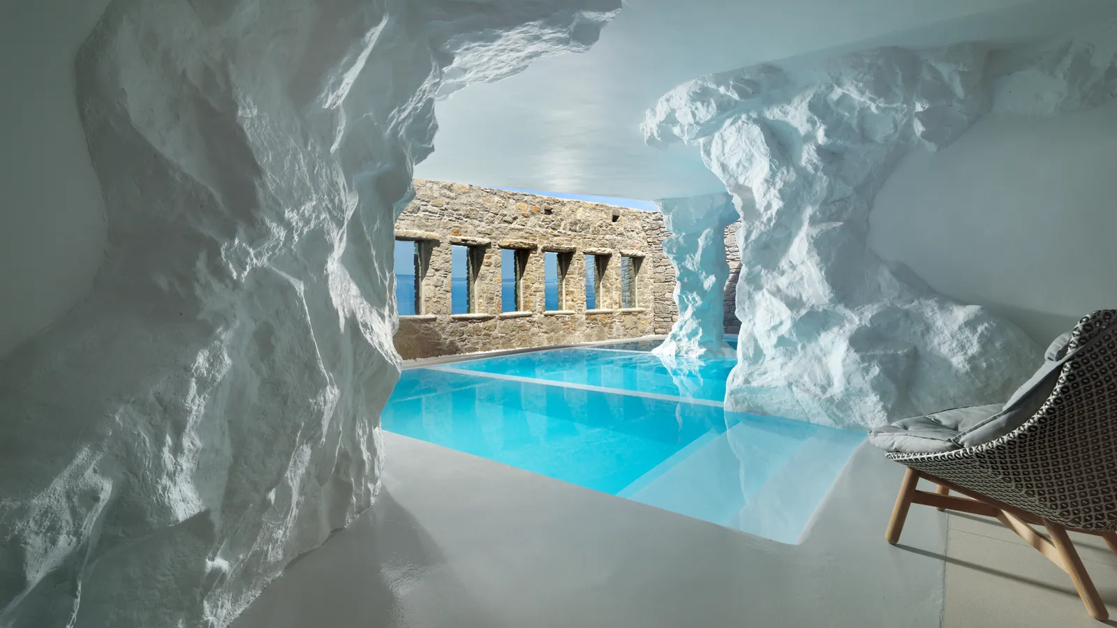 The cave pool of the 2-bedroom suite without a view: white rock, turquoise water, an armchair and a stone wall with openings.