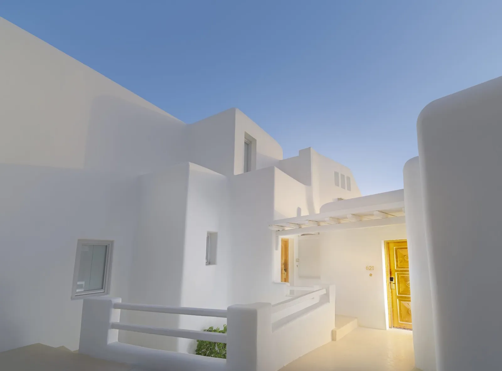 The hotel’s white cubic buildings against the sky, with a stairway, masonry parapets and a gilded door in the sun.