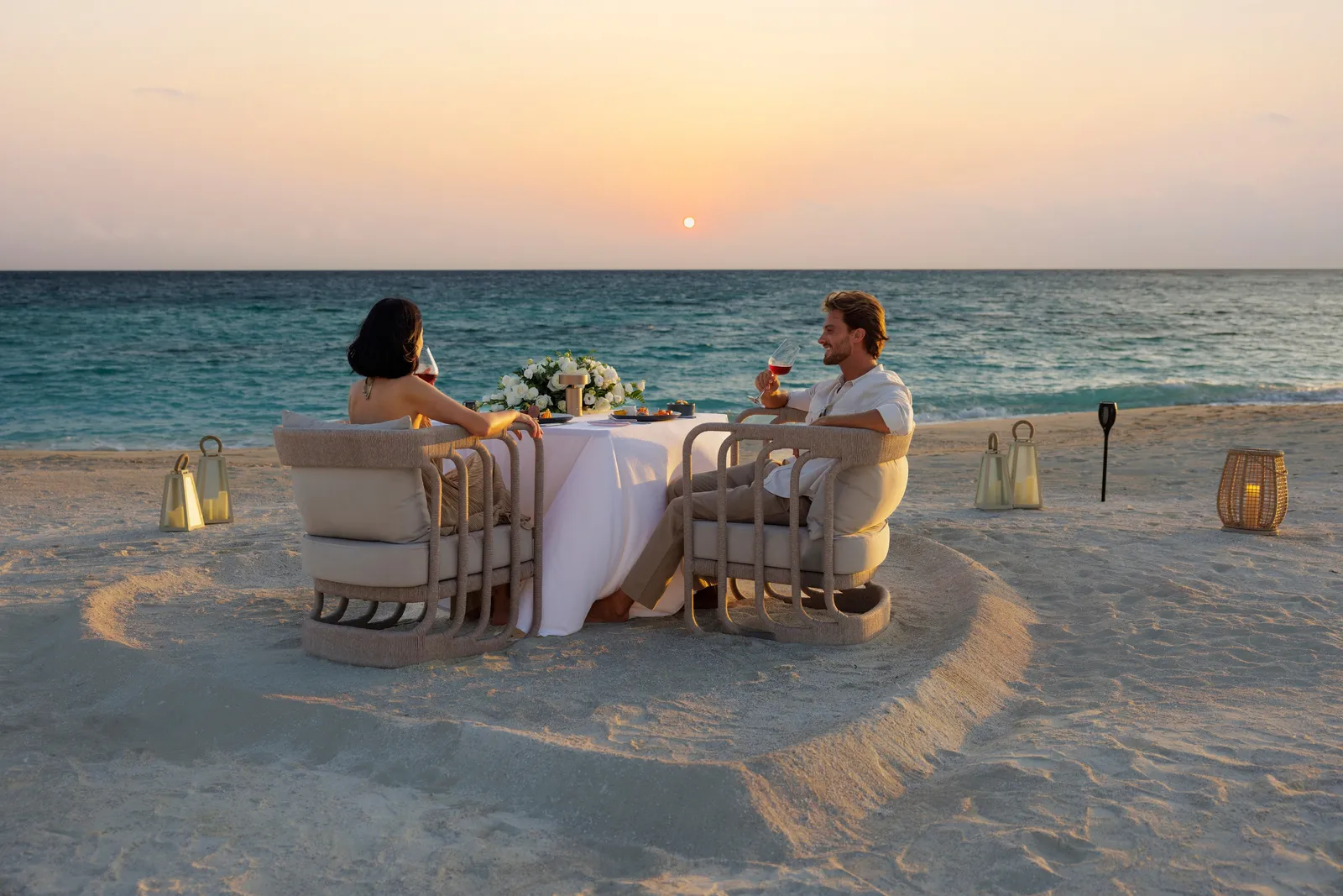 Dinner for 2 on the beach at sunset, the table set in the sand among lanterns