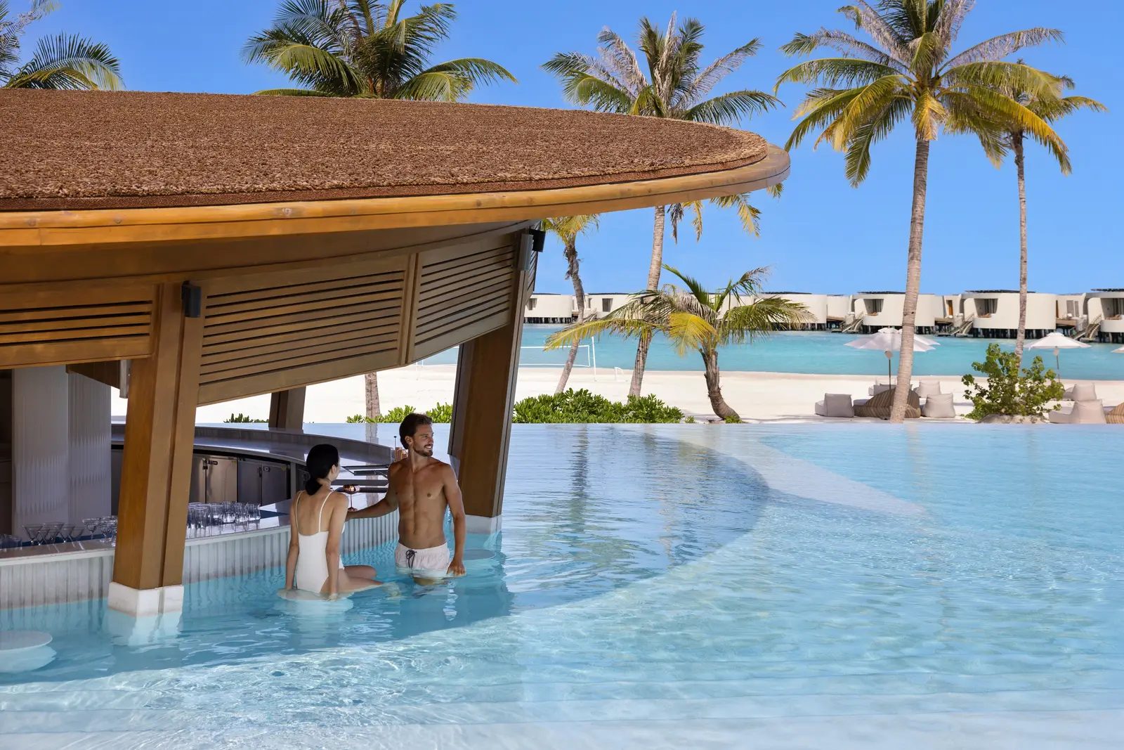 Coco Drift’s swim-up bar under its curved wooden roof, 2 guests sitting in the water