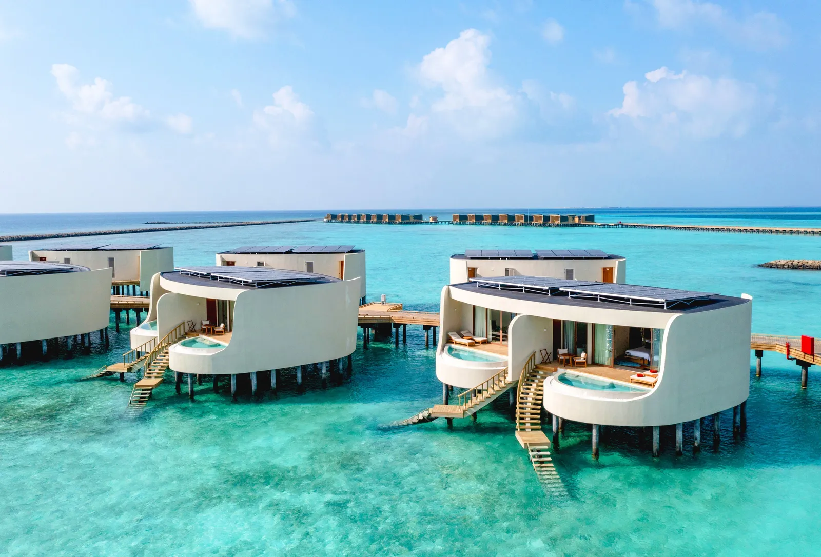Water villas with curved white walls, each with its pool and steps down into the lagoon