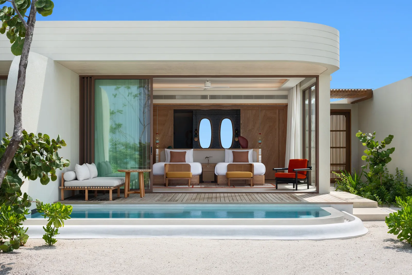 The front of a Sunset Beach Pool Villa: the pool before it, curved white walls, loungers
