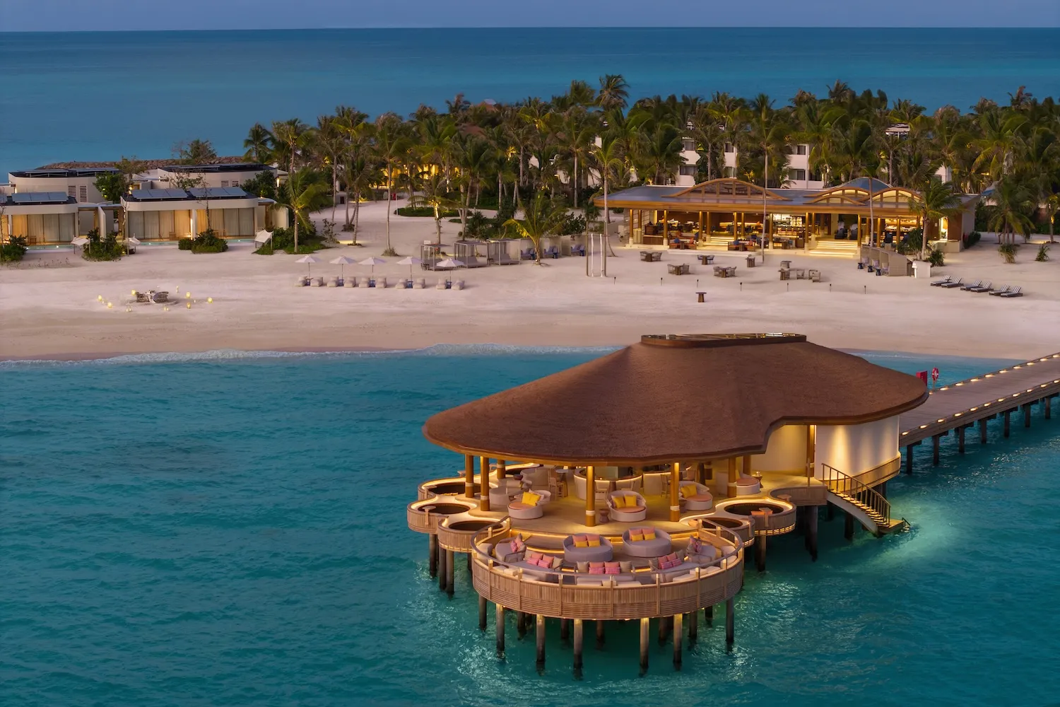 Sunset Social at dusk, the round pavilion over the water and the palm-lined beach behind