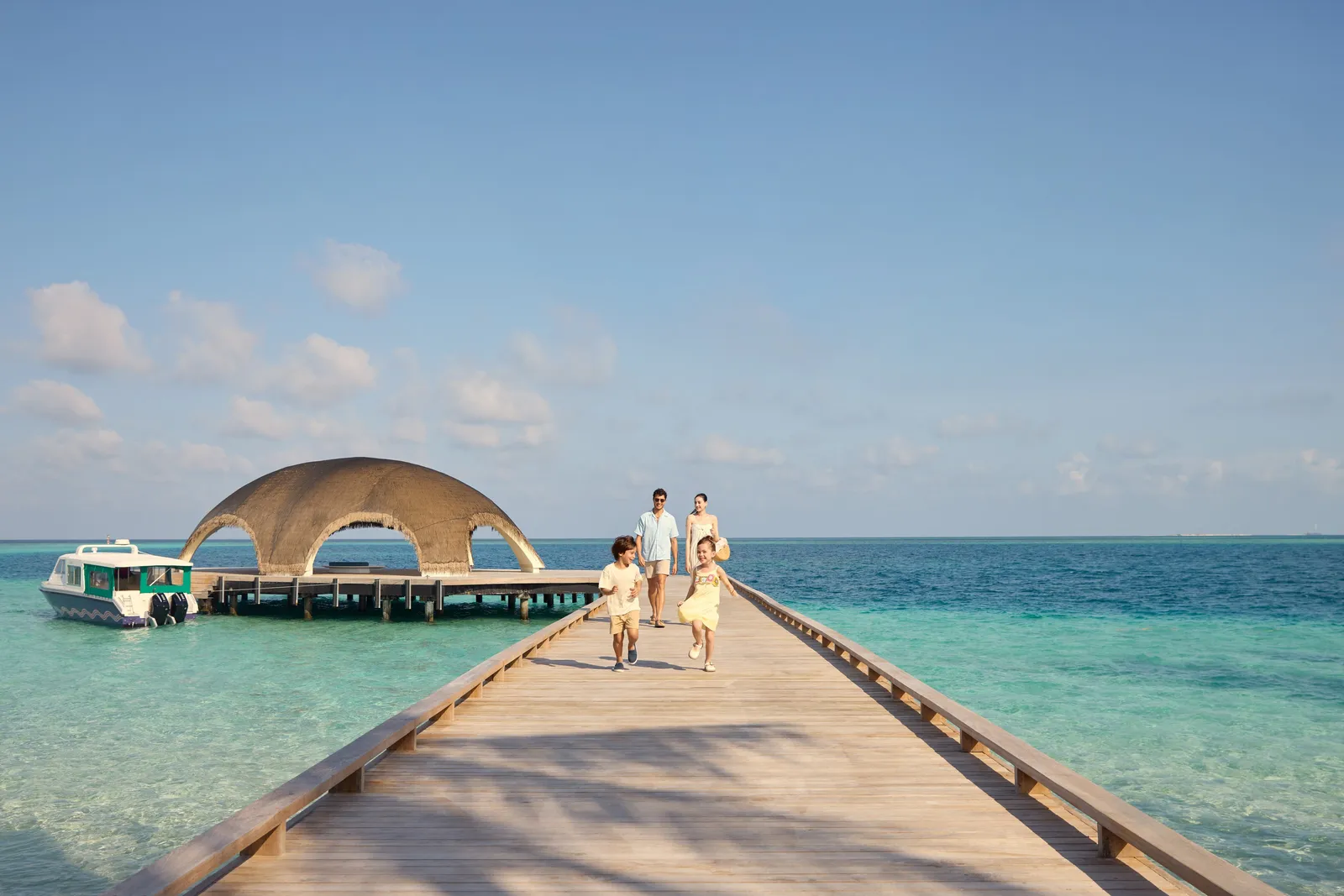 A family on the arrival jetty, the wooden dome and the speedboat moored on the turquoise lagoon