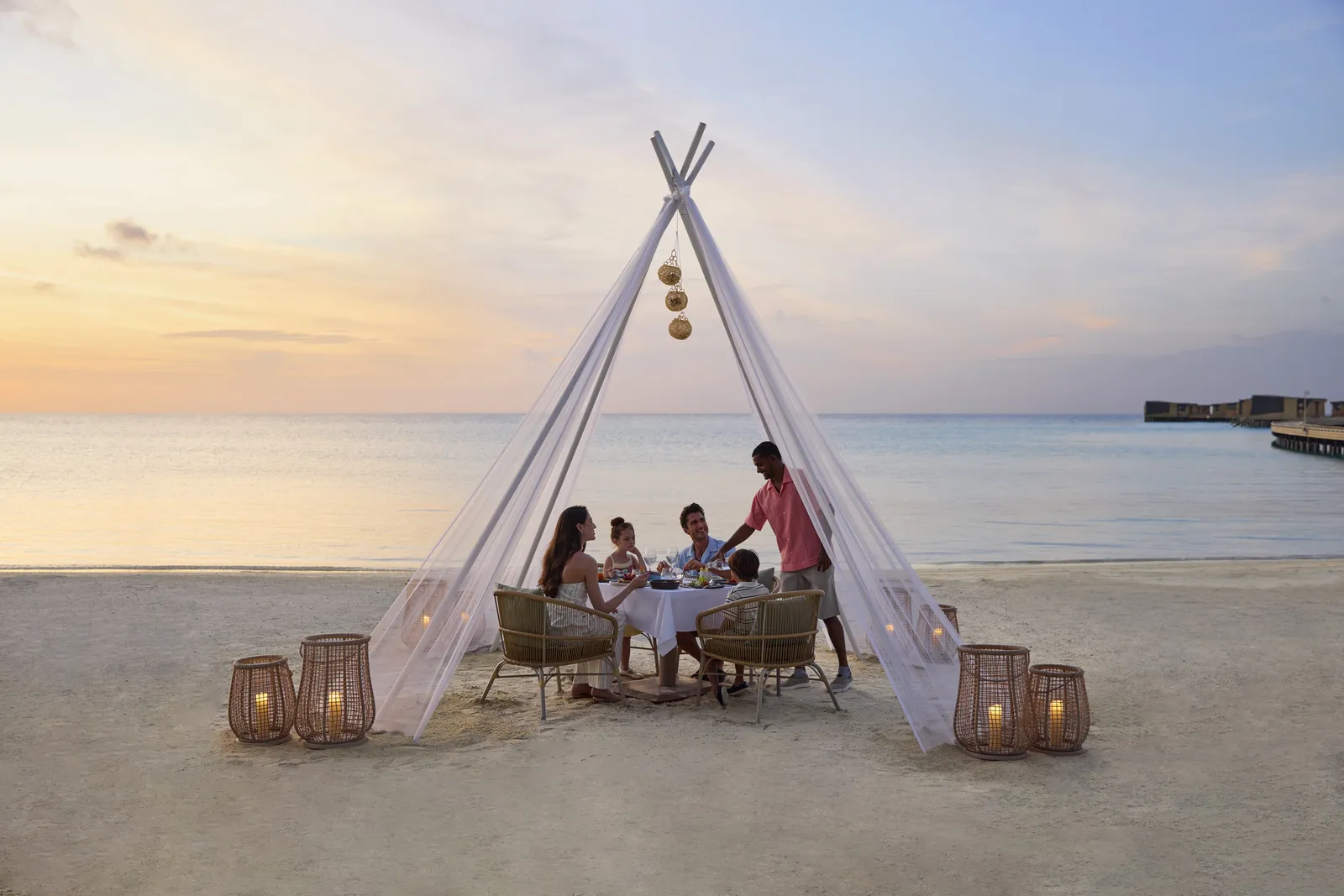 A beach dinner under a white tent at sunset, among lanterns