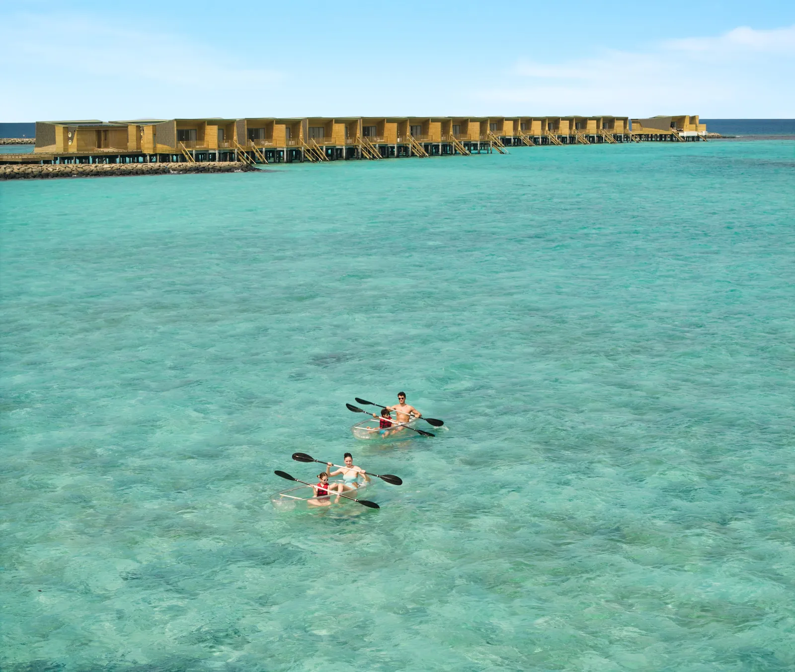 2 clear kayaks with parents and children on the lagoon, the water villas beyond