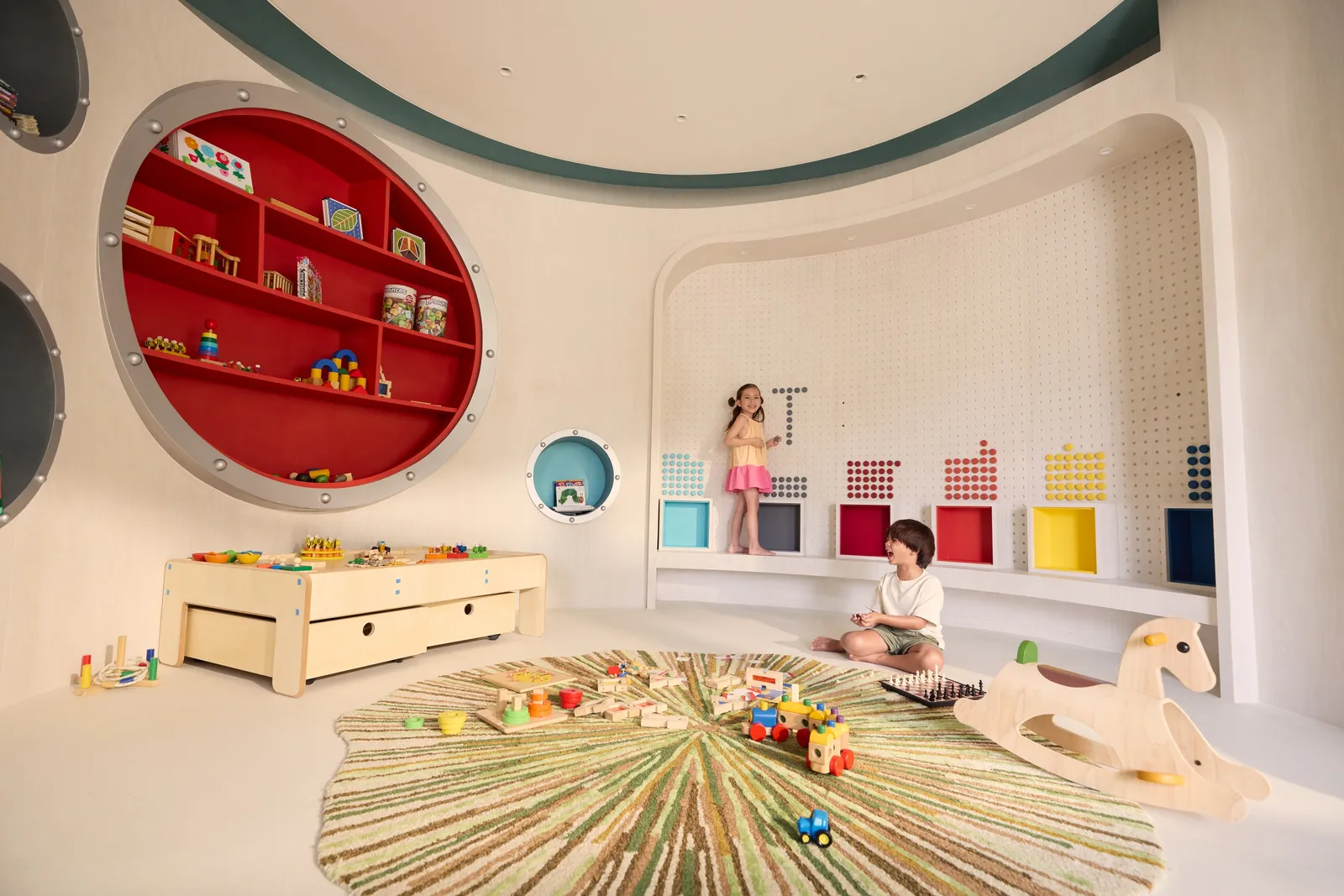 The Kids’ Club room, its big red porthole full of toys and 2 children on the rug