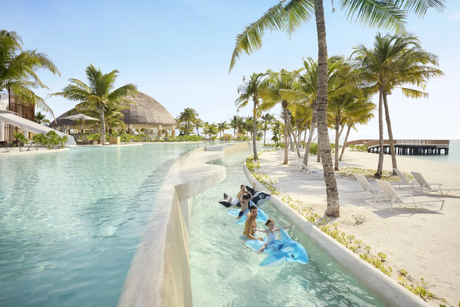 Children on rubber rings along the lazy river, the thatched dome and palms behind