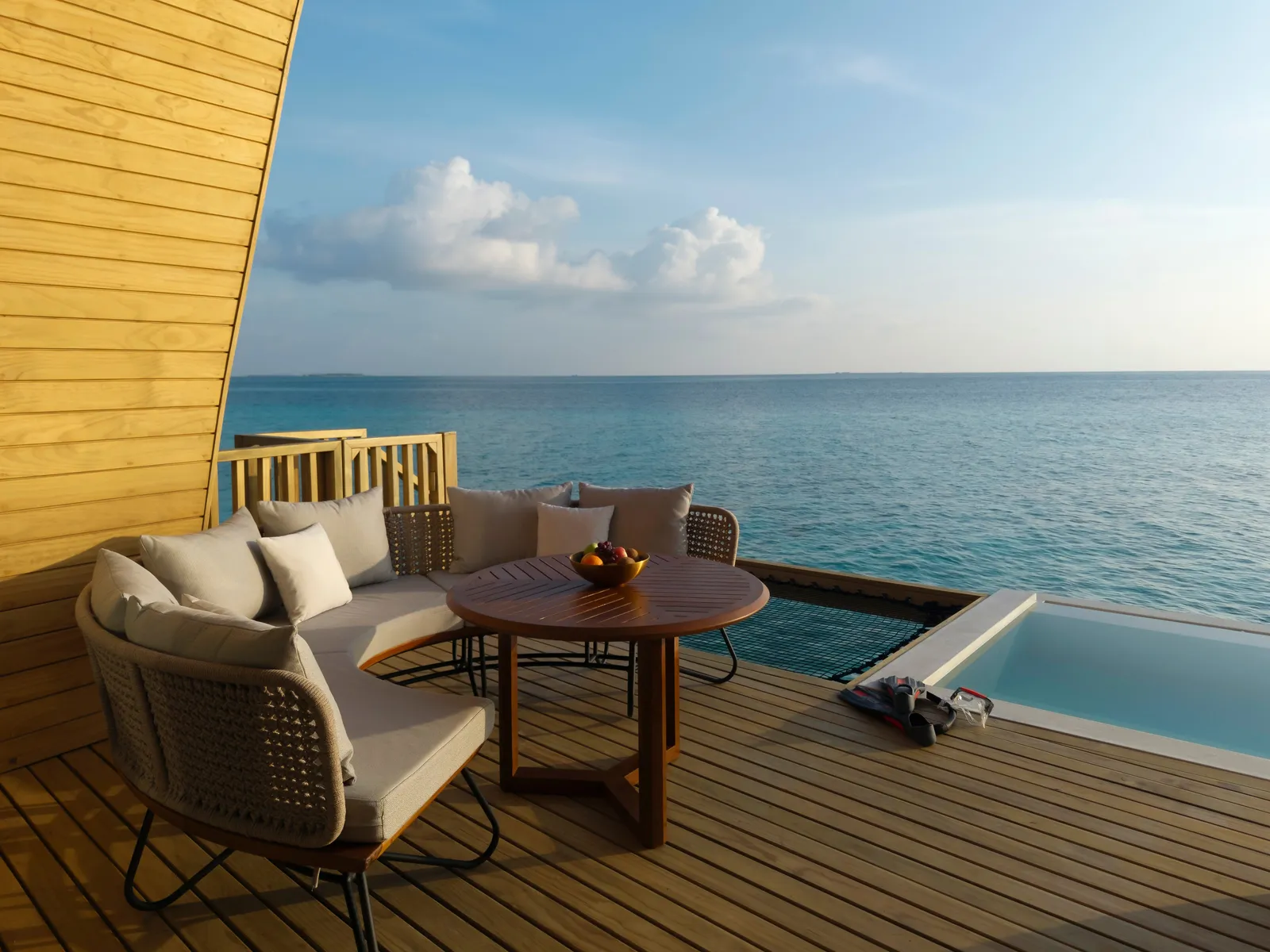 The outdoor lounge of a Mirage Overwater Sunrise Pool Villa, beside its pool above the sea