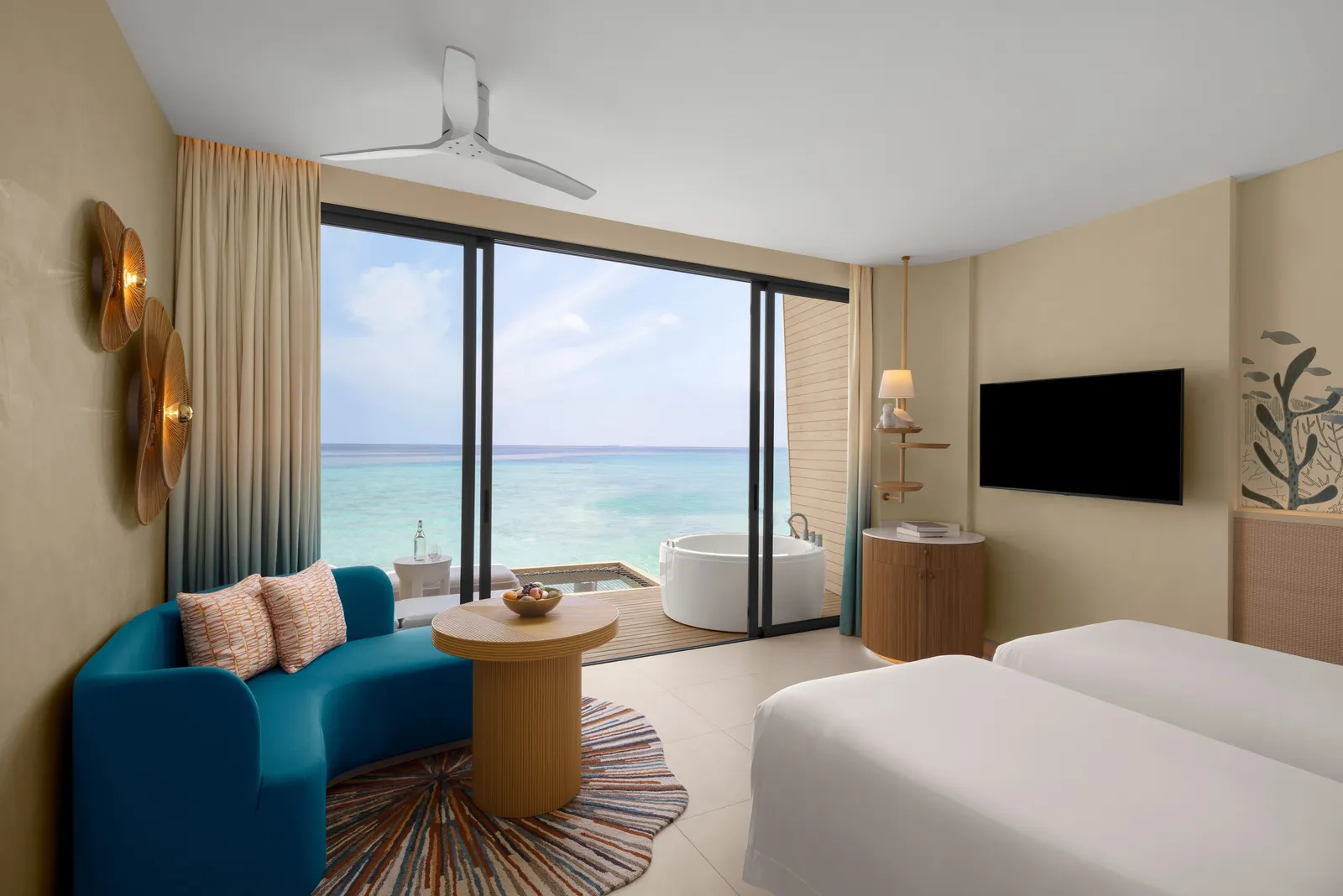 An Overwater Villa with Jacuzzi: the blue sofa, the bed and the glass wall on the sea
