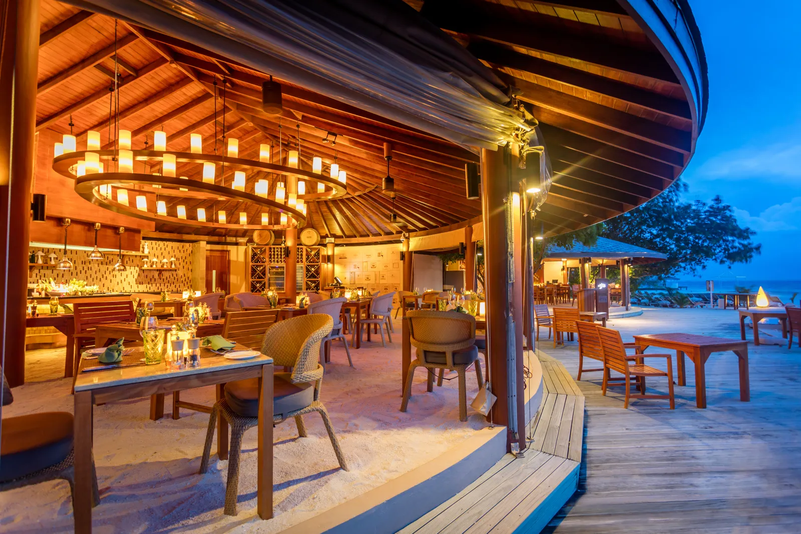 La Brezza at nightfall: the chandelier under its timber roof, the sand floor and tables looking out to the lagoon.