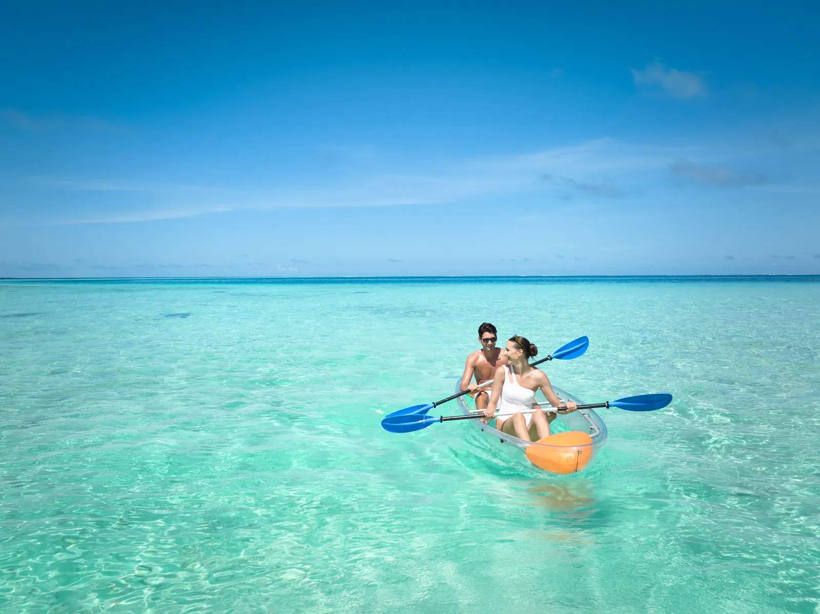 2 guests in a clear kayak on the lagoon, over shallow, glassy water.