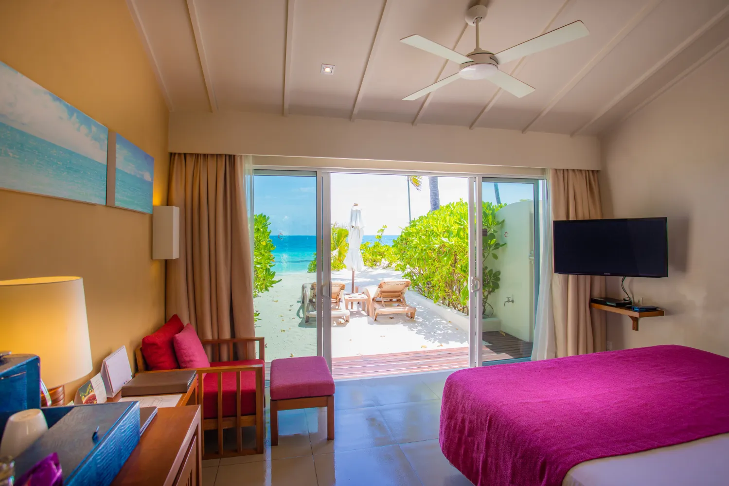 A Lagoon View Beach Villa: the bed, the armchairs and the glass doors open on to the terrace and the beach.