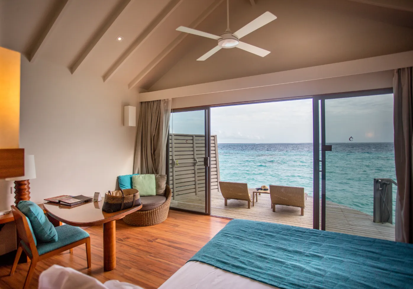 An Overwater Villa: the bed, the sitting area and the glass doors open on to the deck above the sea.