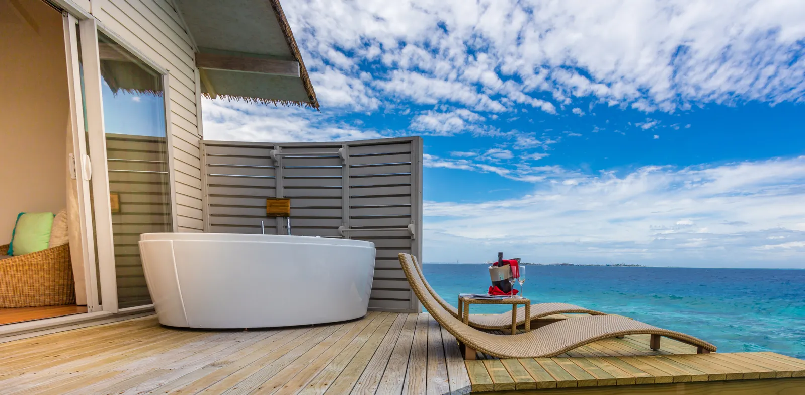 The deck of an Overwater Villa with Swirl Pool, its white spa tub and a lounger above the ocean.