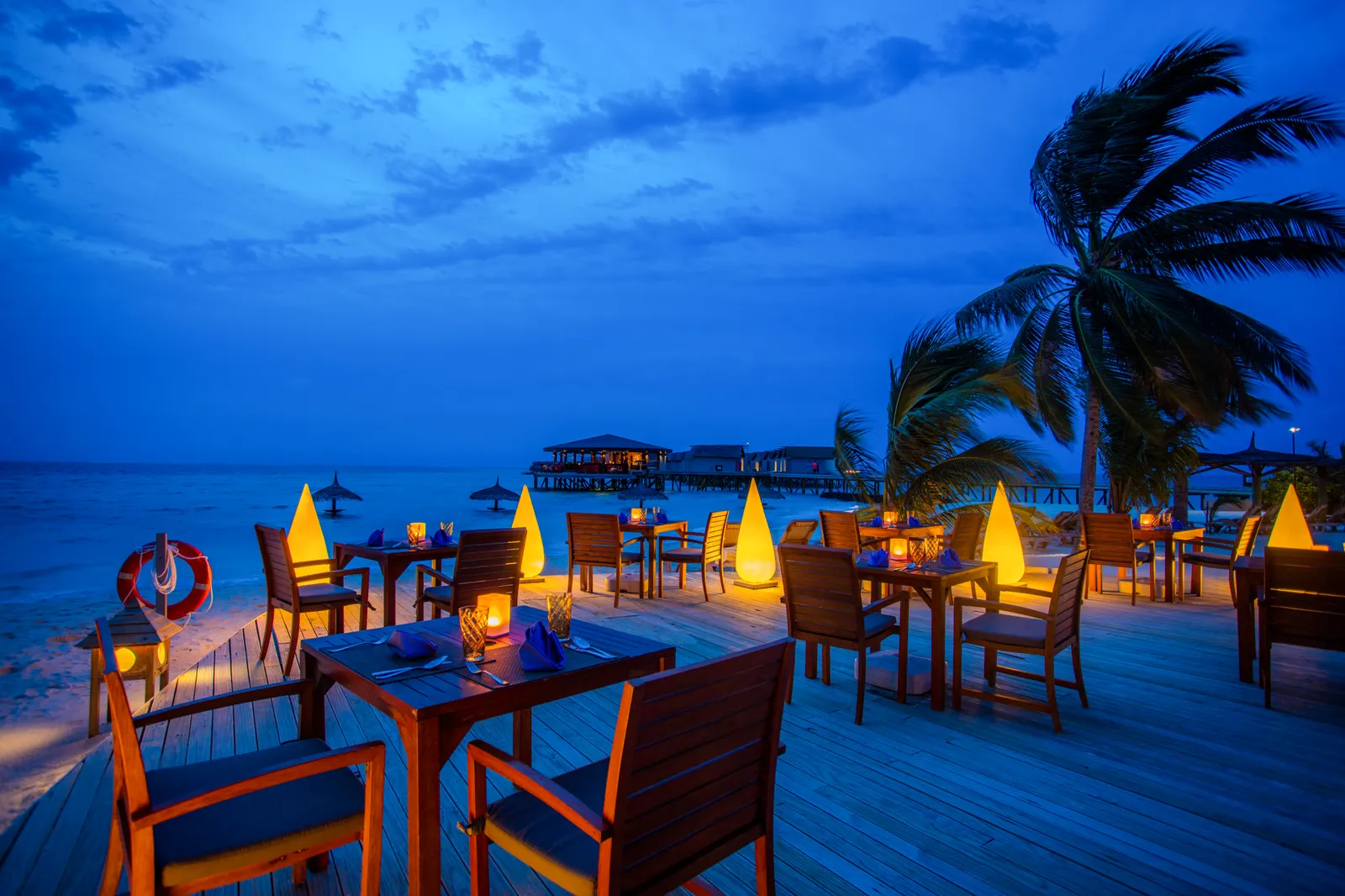 Suan Bua’s terrace in the evening, lanterns on the tables and the lit jetty behind.