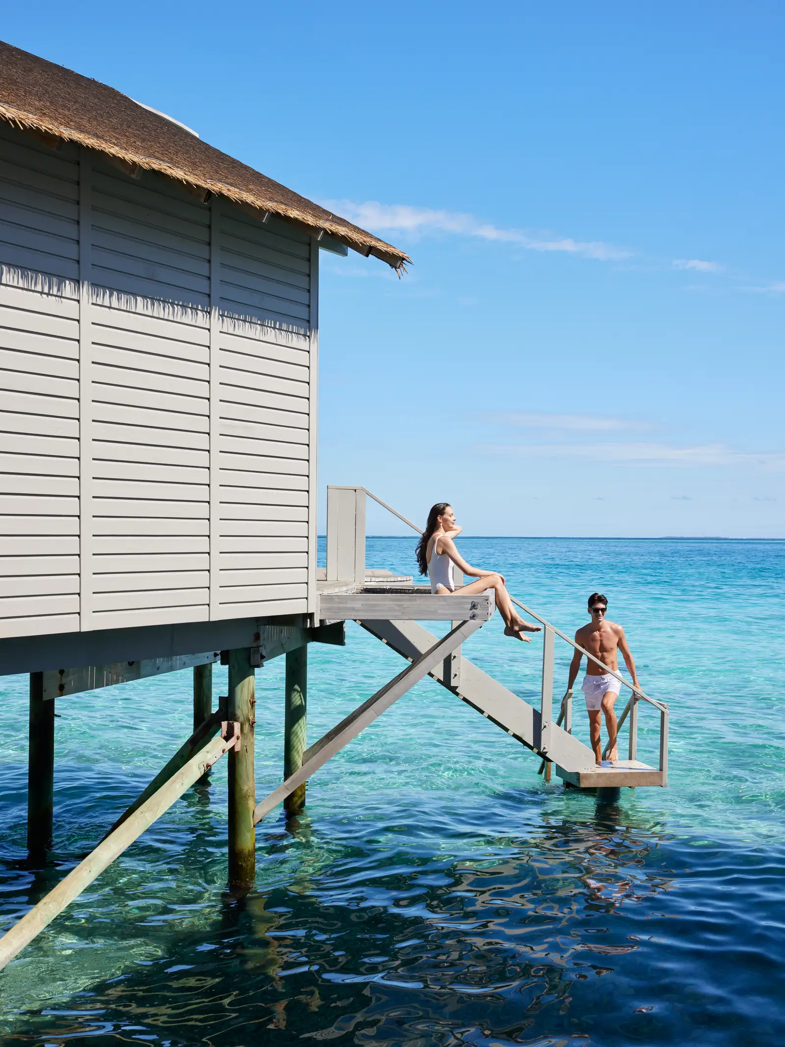 A couple on the steps of a water villa, which lead straight down into the lagoon.