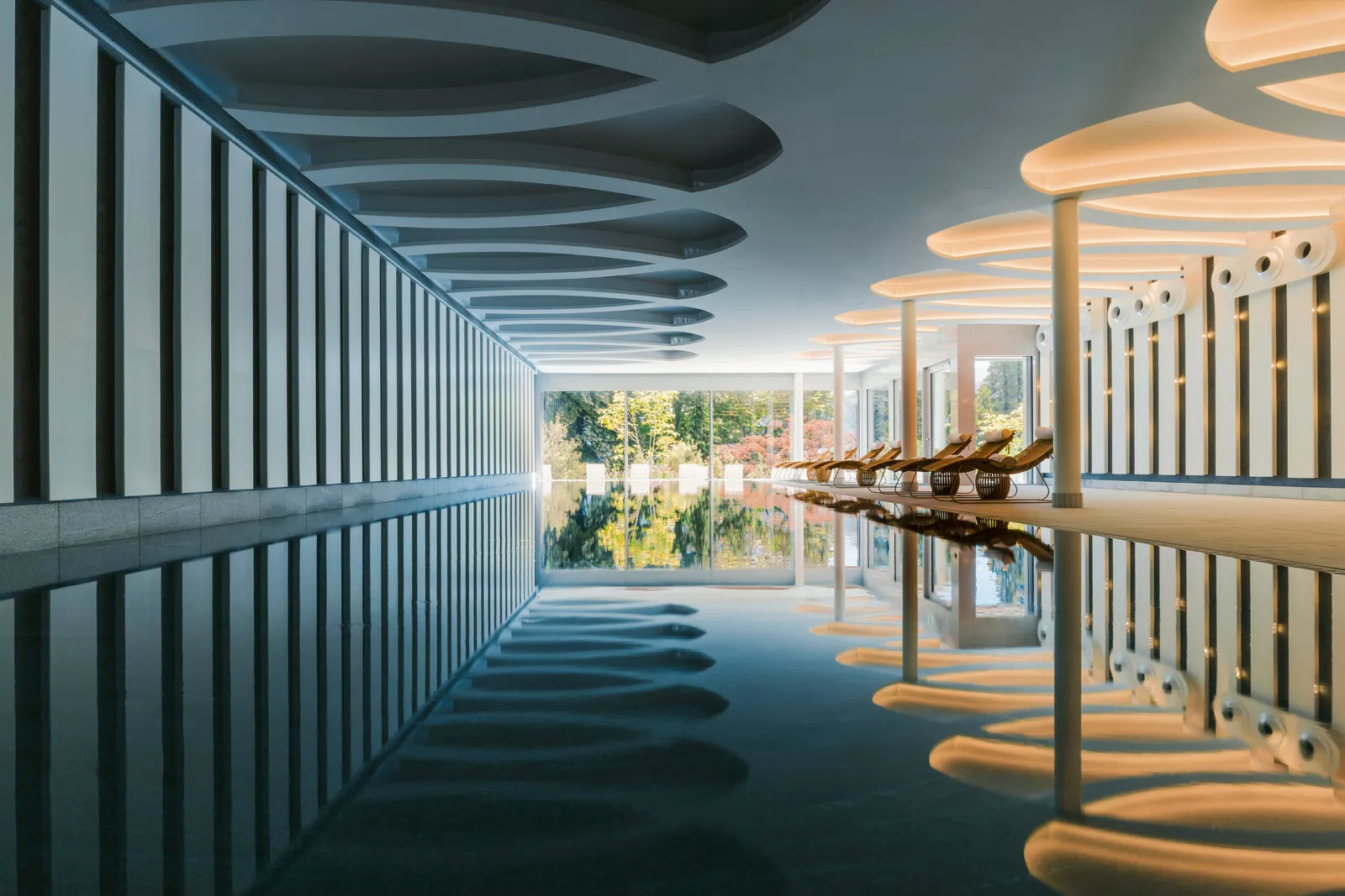 La piscina coperta con le sdraio sul fondo e il giardino oltre le vetrate