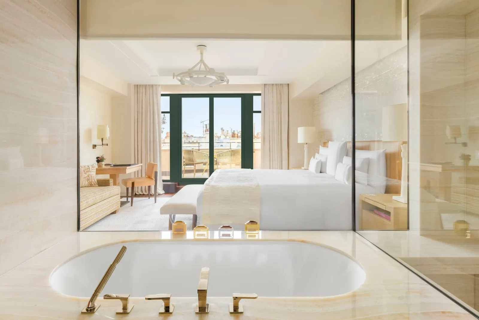 A bathroom with a bath and bedroom beyond a glazed wall