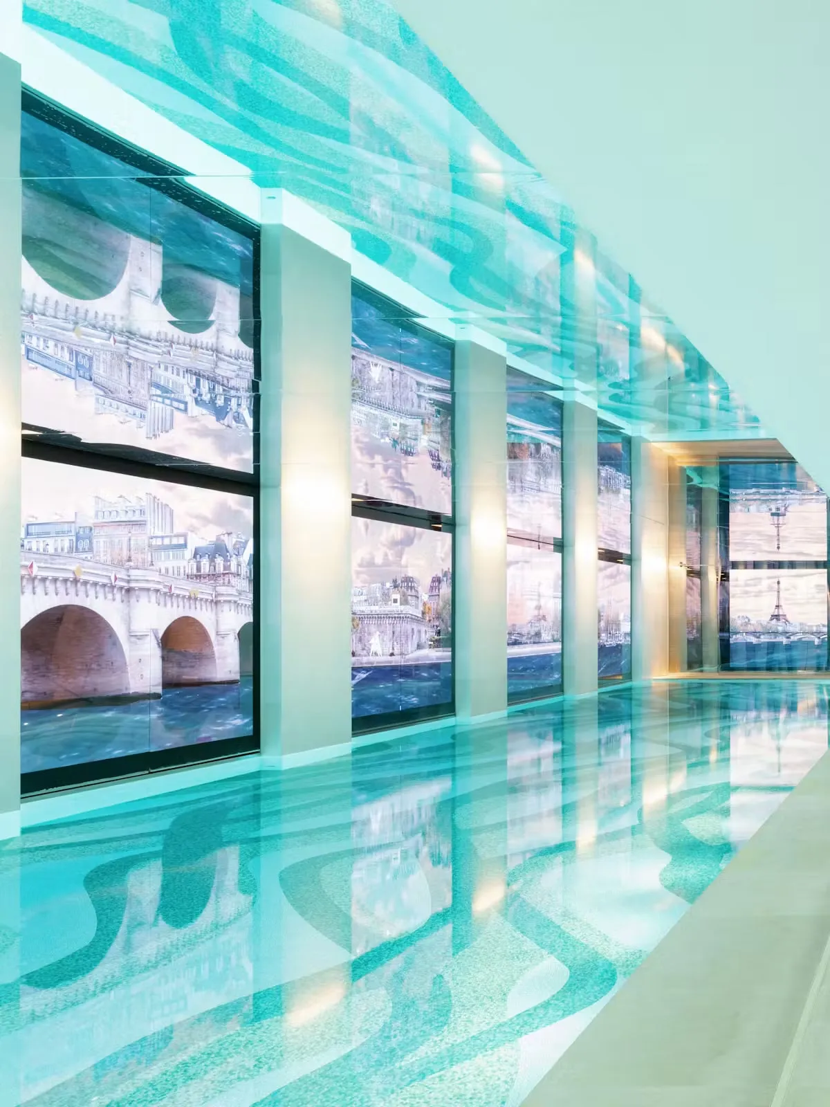 An indoor pool and white loungers before an image wall