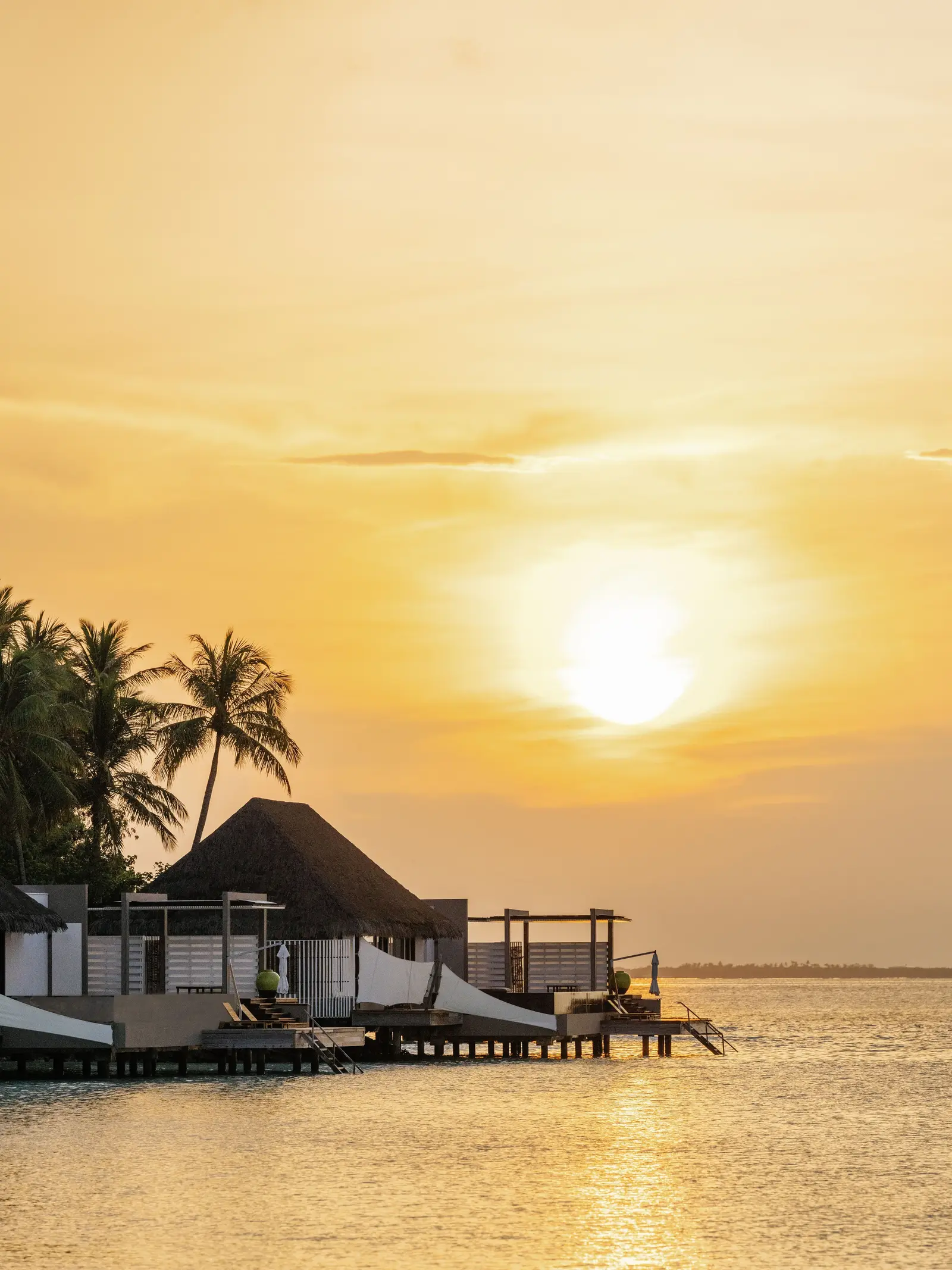 Sunset over the lagoon, a water villa against the light