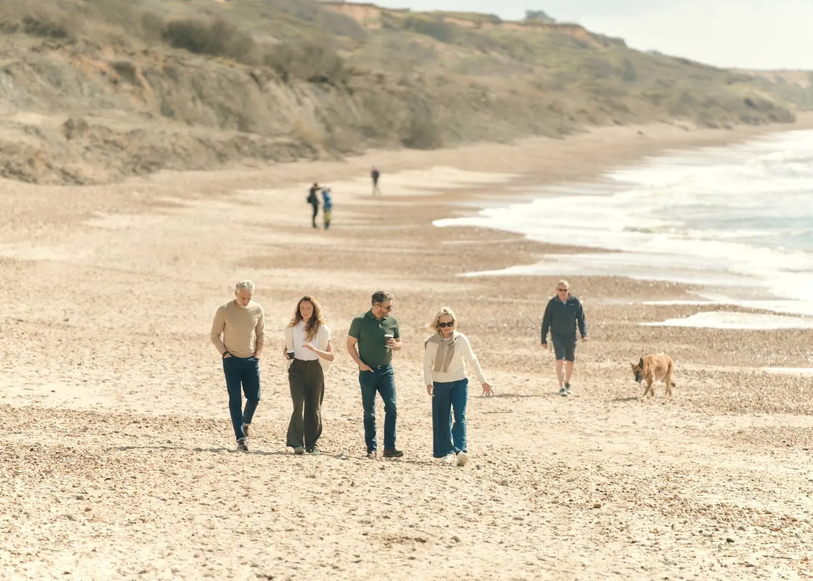 Guests walking on the beach below the cliffs, with a dog