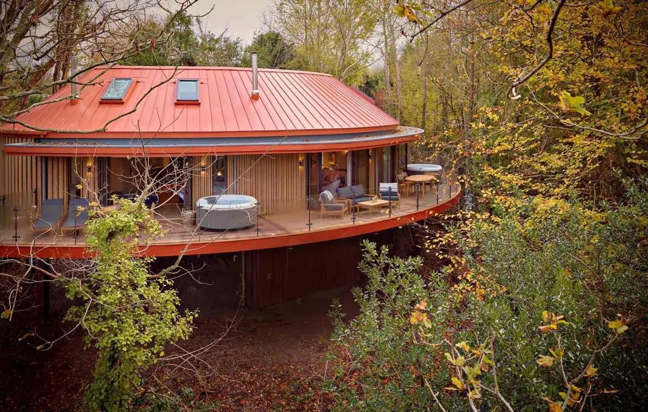The Yews, the curved treehouse with its terrace and hot tubs in autumn trees