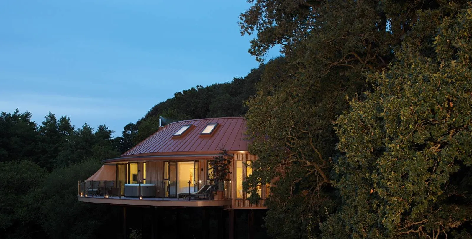 The Hideaway Suite at dusk, lit up, its terrace among the trees