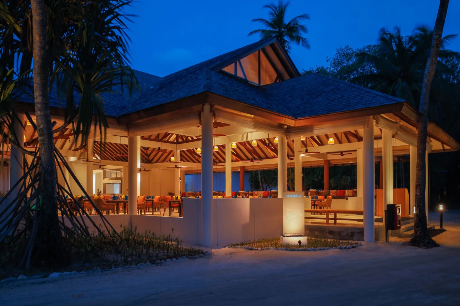 Koimala lit up in the evening, its glass doors open among the palms