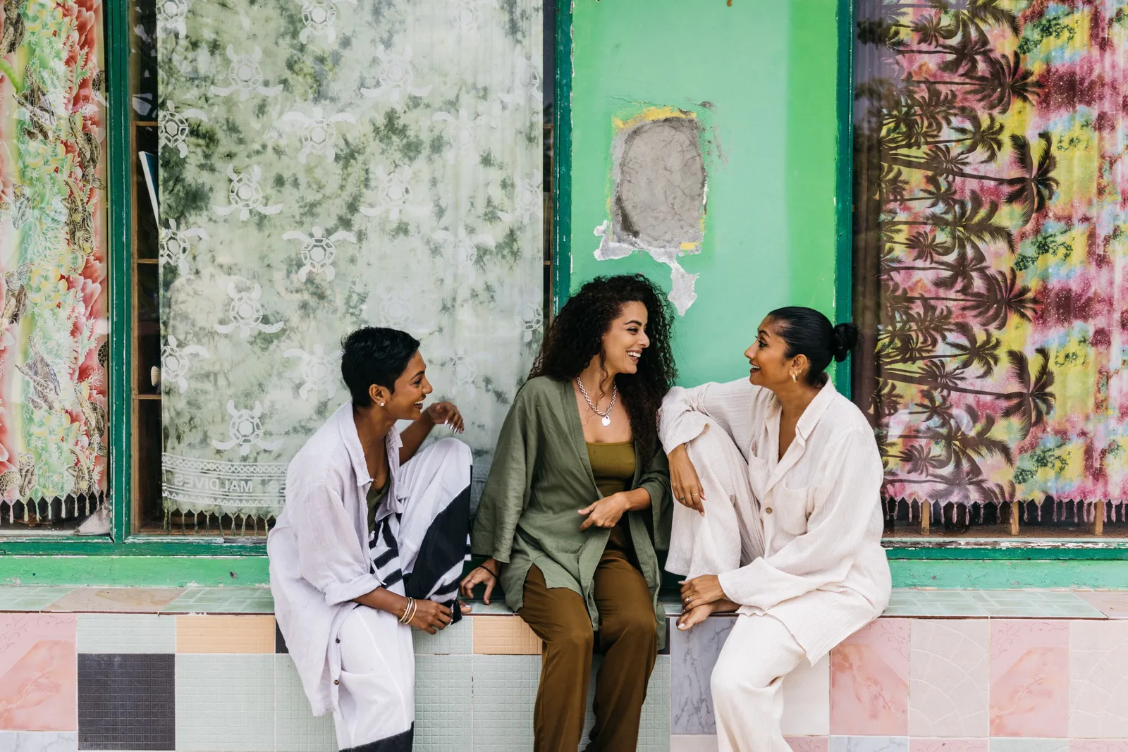 3 people talking beside the green façade of a house on a local island