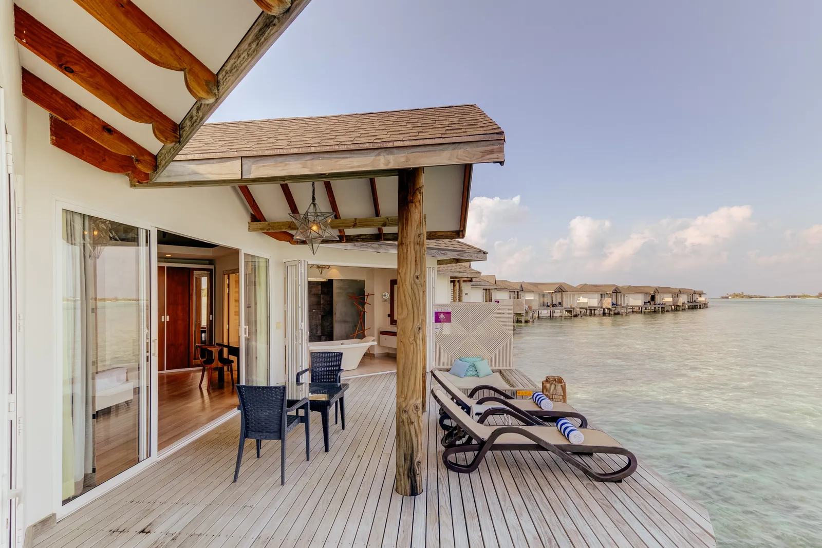 An Over Water Suite’s terrace with a table and loungers above the lagoon