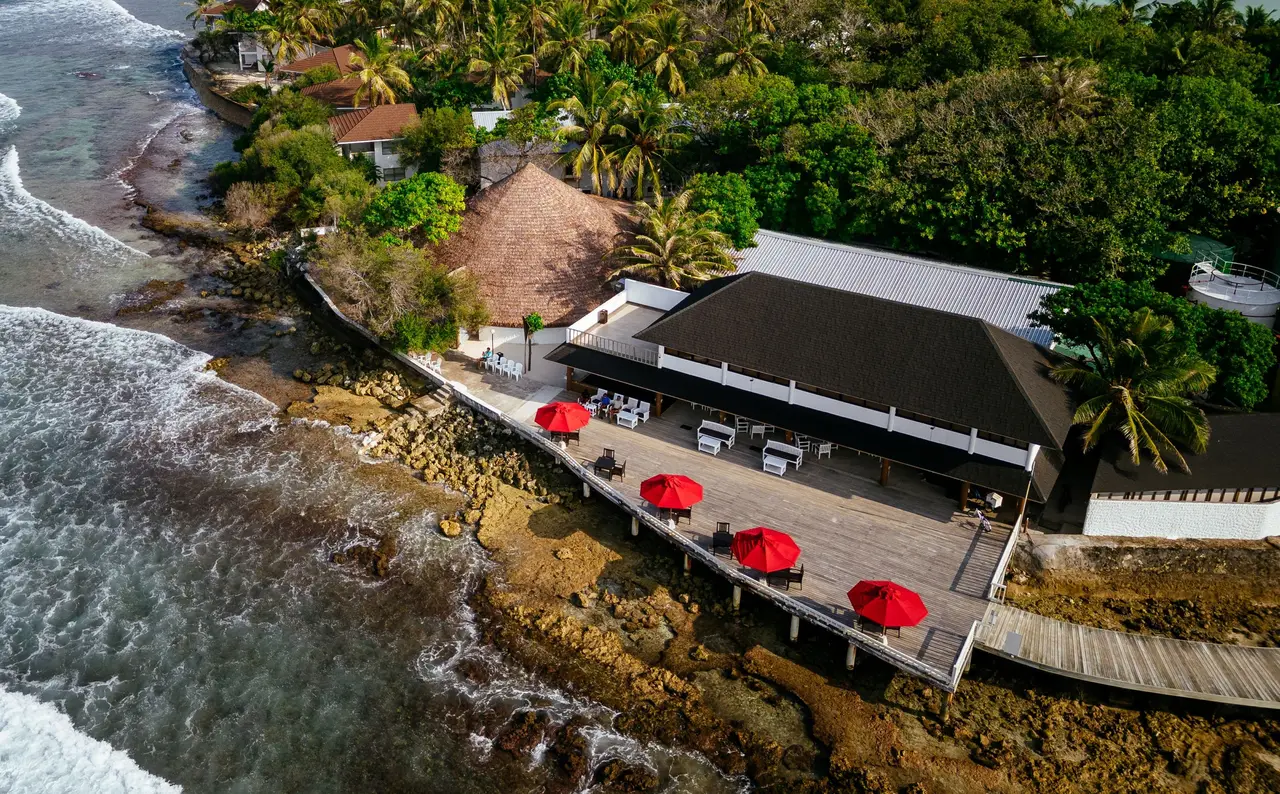 The Raalhu Bar from above, red parasols on its deck beside the reef