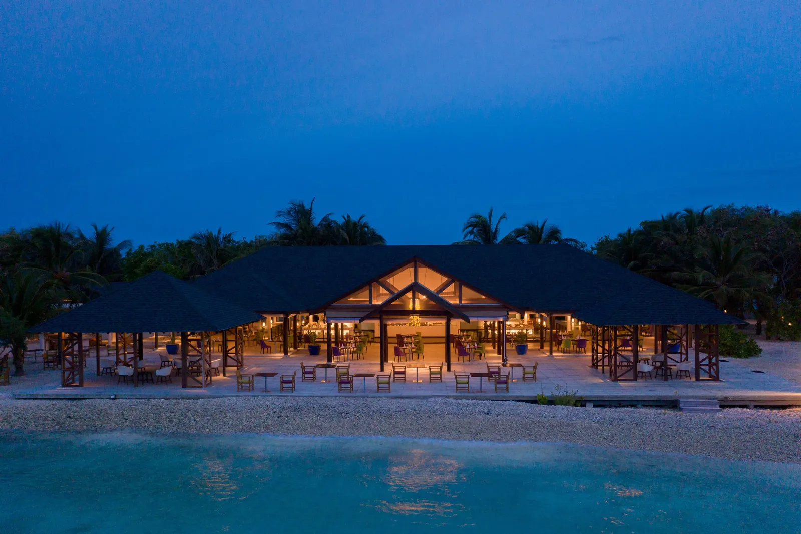 Rehendhi restaurant lit up at dusk among the palms