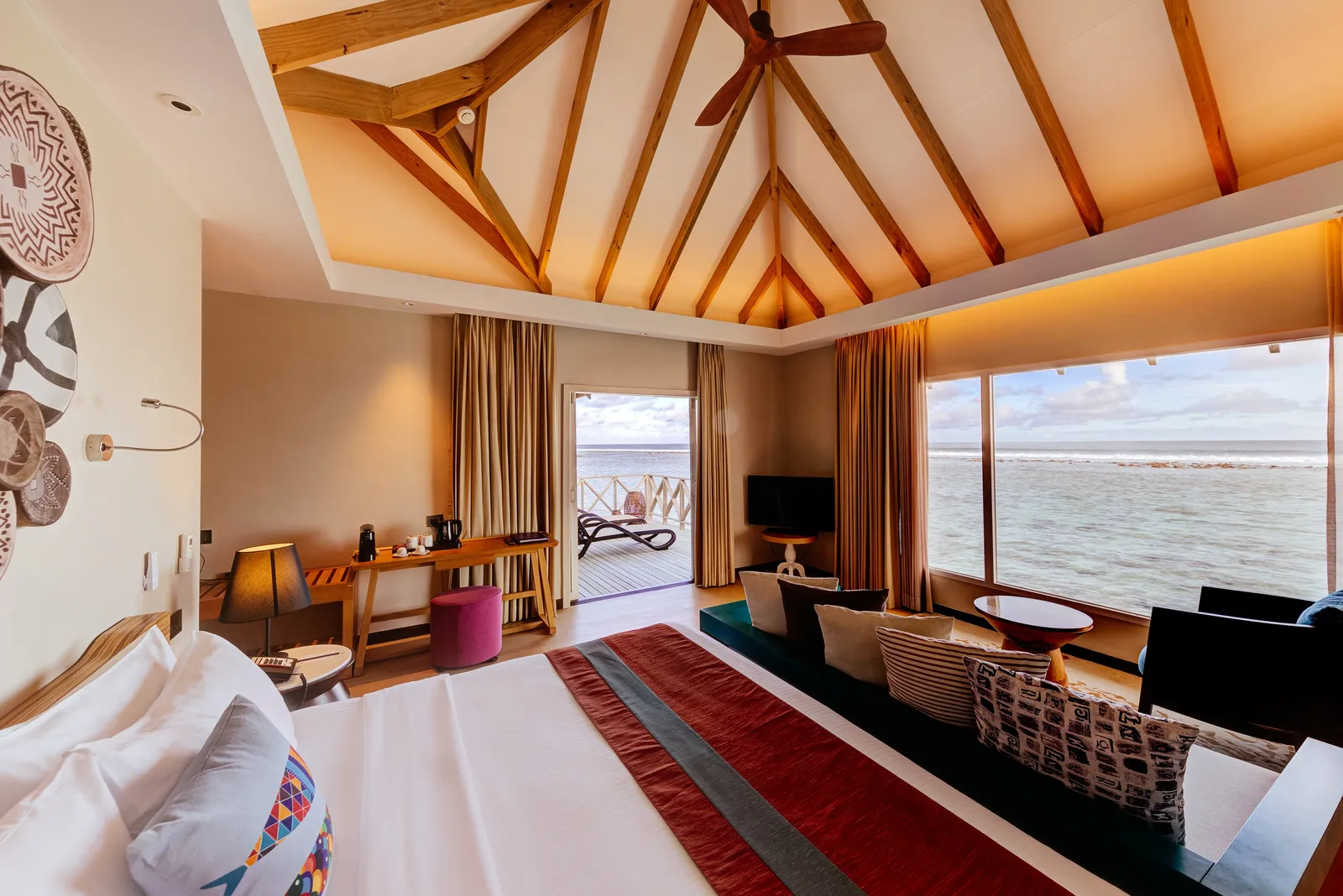 A Water Bungalow bedroom, its bed beneath the timber roof and door opening towards the lagoon