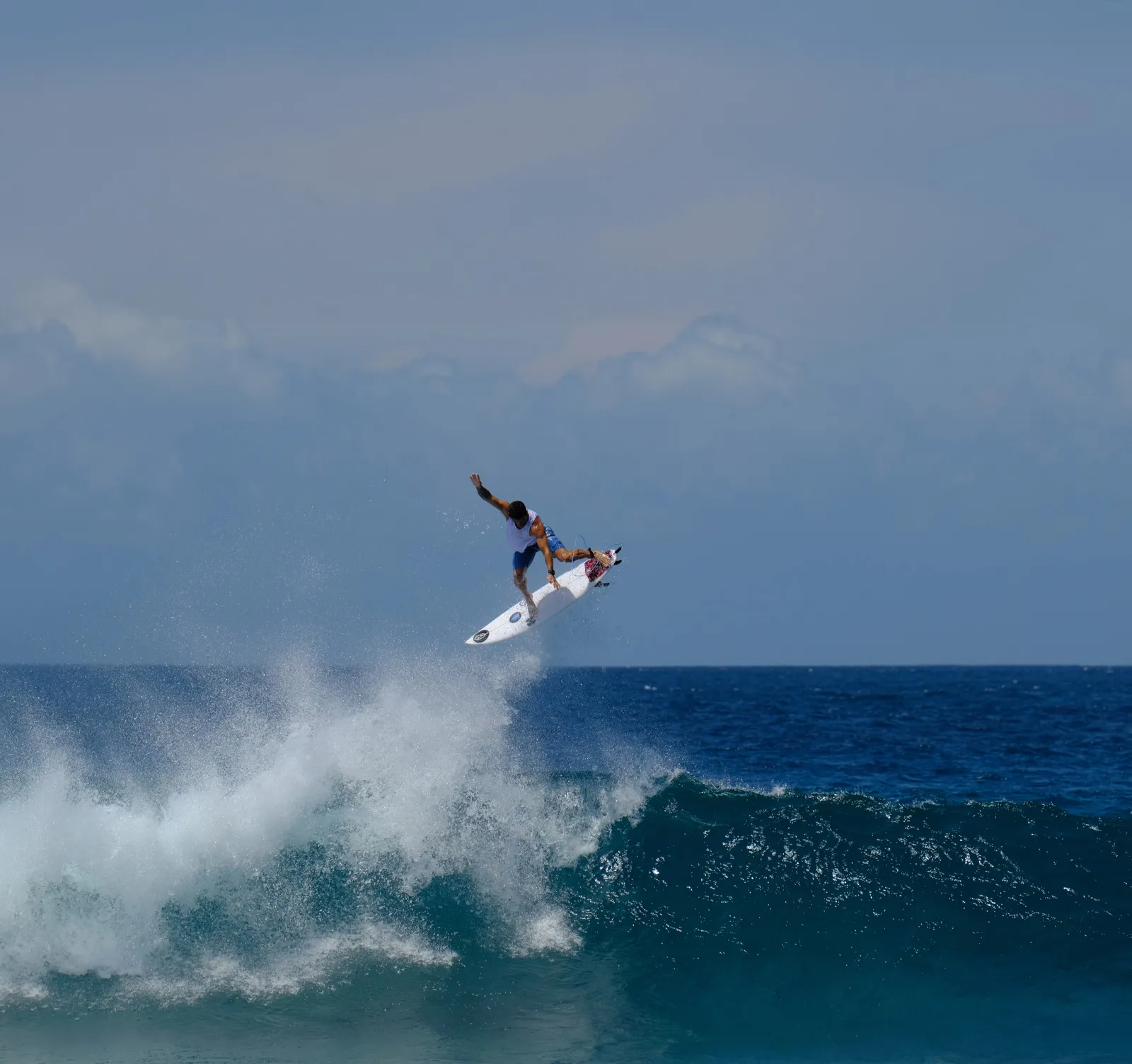 A surfer lifting his board above the crest of a wave