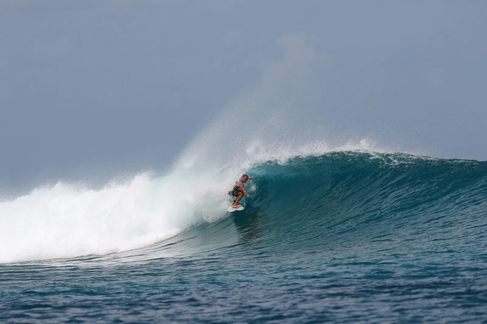 A surfer riding the face of a wave beneath its breaking crest