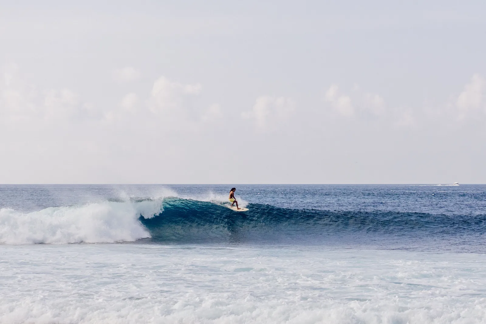 A surfer riding a long wave breaking over the reef