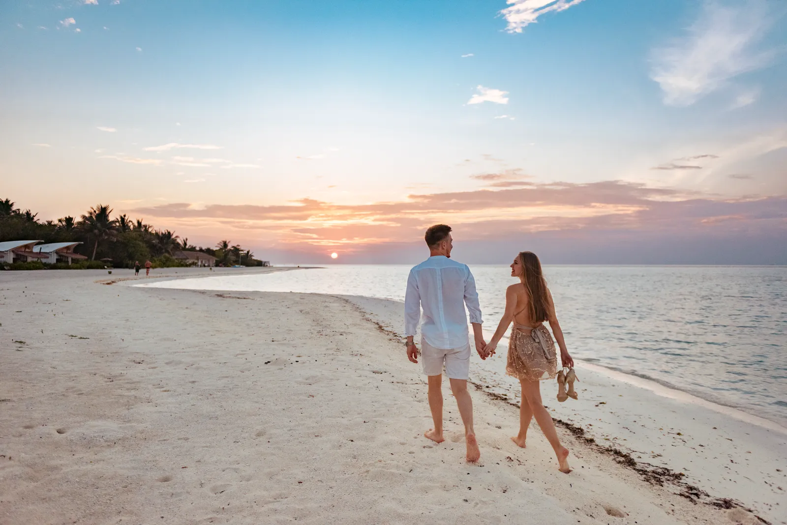 A couple walking barefoot along the beach at sunset