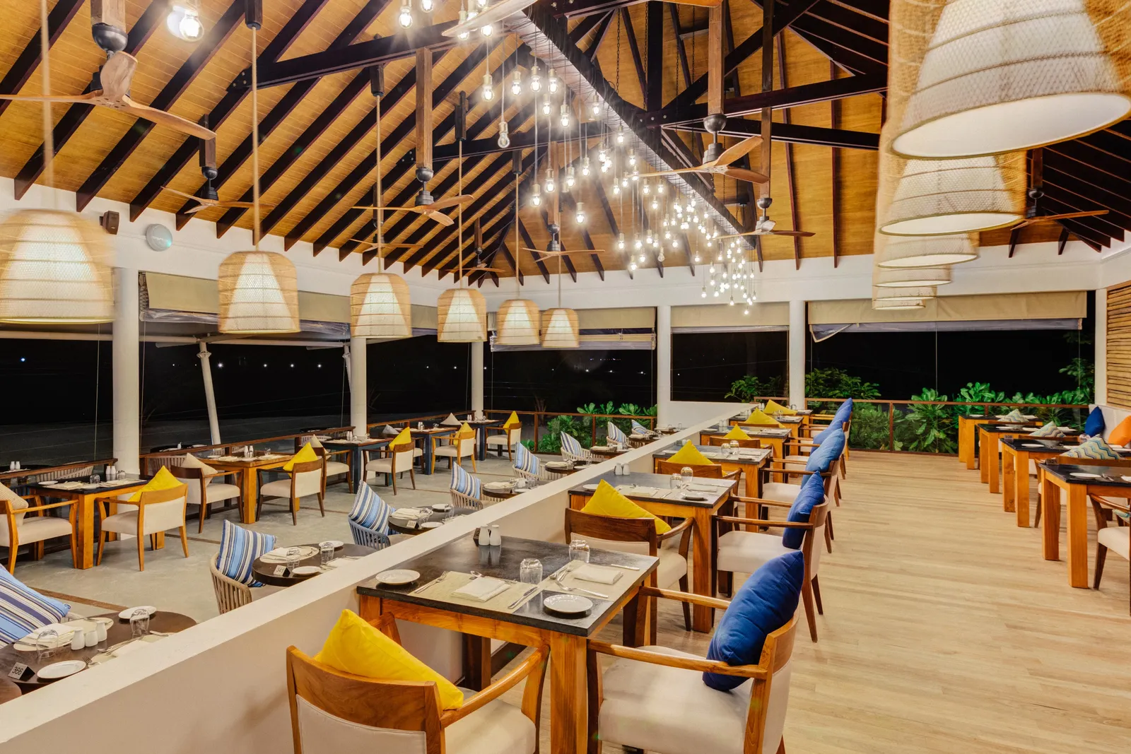 Malaafaiy’s dining room in the evening: rows of tables under the timber roof and woven lamps