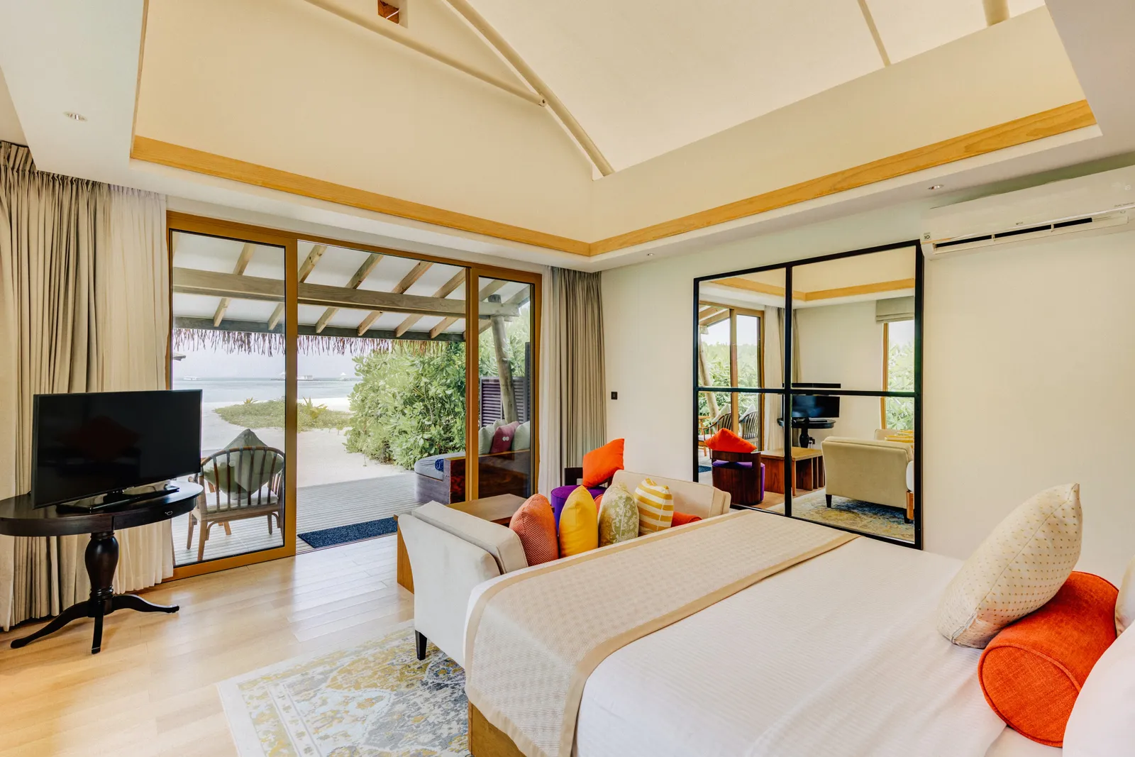 A Beach Bungalow bedroom: the bed with its orange cushions and the glass door open to the beach